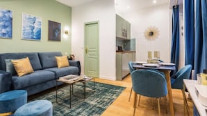 A modern living room with a sofa, coffee table, and chairs, a dining area with a table and chairs, and a kitchen in the background. - 3. cosy 1BR - Père Lachaise - Nation (Paris)