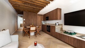 A modern kitchen with wooden cabinets, a dining area with a round table and chairs, and a flat-screen TV mounted on the wall. - Luxury - 1BR - Louvre/Saint Honoré/palais Royal-AC (Paris)