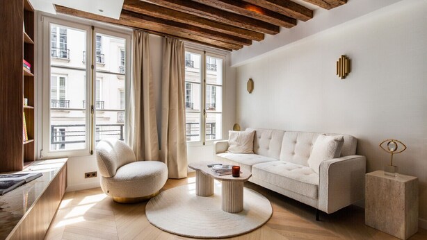 A modern living room with a sofa, armchair, coffee table, and a view of buildings through large windows. - Luxury - 1BR - Louvre/Saint Honoré/palais Royal-AC (Paris)