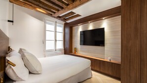 A modern bedroom with a large bed, wooden ceiling beams, a mounted TV, and a window. - Luxury - 1BR - Louvre/Saint Honoré/palais Royal-AC (Paris)