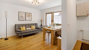 Una sala de estar moderna con un sofá gris, piso de madera, una mesa de comedor y una lámpara en el techo.