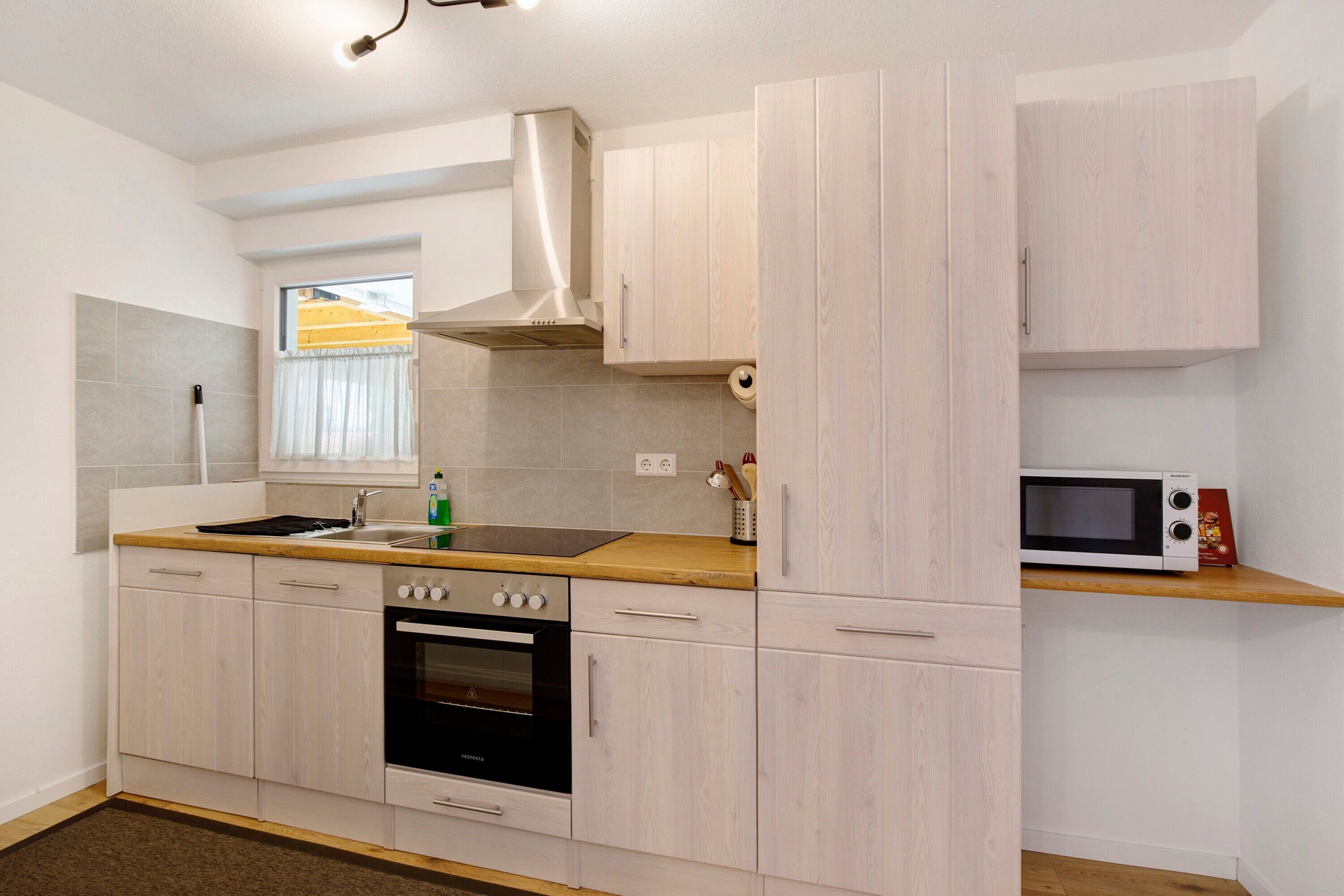 Een moderne keuken met lichte houten kastjes, een roestvrijstalen afzuigkap, een inbouwoven, een magnetron en een houten aanrecht.