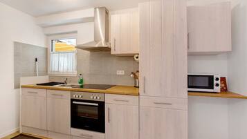 Een moderne keuken met lichte houten kastjes, een roestvrijstalen afzuigkap, een inbouwoven, een magnetron en een houten aanrecht.