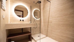 A modern bathroom with a wooden vanity, two round mirrors, a shower area, and a wooden bench.