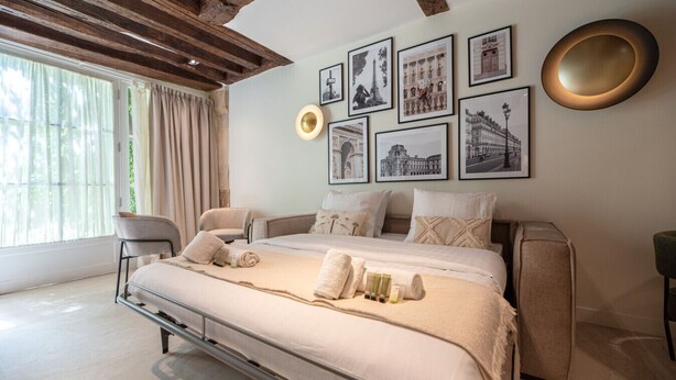 A bedroom with a bed, a chair, a bedside table, and a window with curtains.