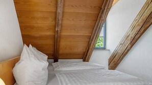 Un dormitorio con techo inclinado, vigas de madera y una ventana.