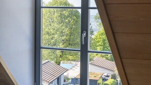 Una habitación con ventana que da a un barrio residencial, techo de madera y sofá gris.