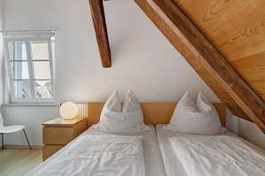 Un dormitorio con techo de madera, una ventana, una mesita de noche y dos camas.