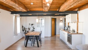 A modern kitchen with wooden beams, a dining area with a wooden table and chairs, and a view of the adjacent room. - Apartment 'Steigen' with Wi-Fi (Heiligenberg)