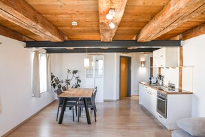 Una cucina moderna con travi in legno, una zona pranzo con tavolo e sedie in legno, e vista sulla stanza adiacente.