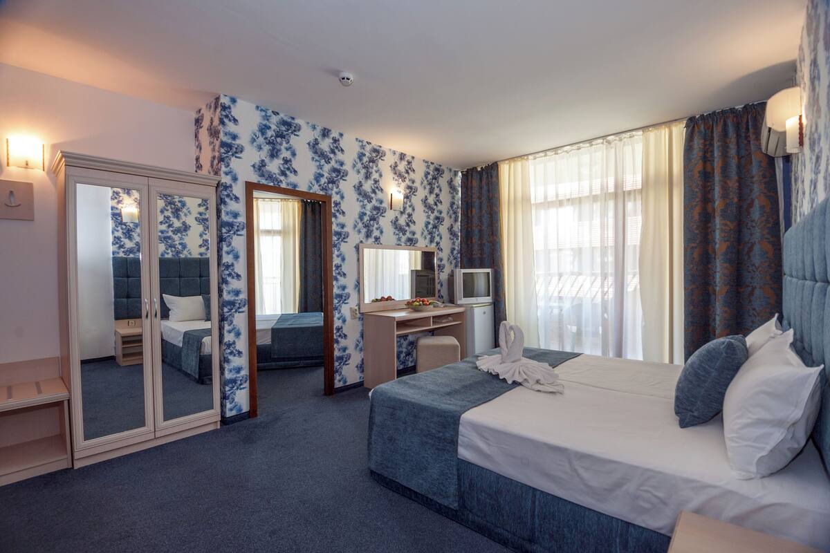 A hotel room with a bed, a desk, a wardrobe, and a mirror.