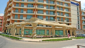 Ein mehrstöckiges Hotel mit Balkonen und einer markanten Skulptur davor.