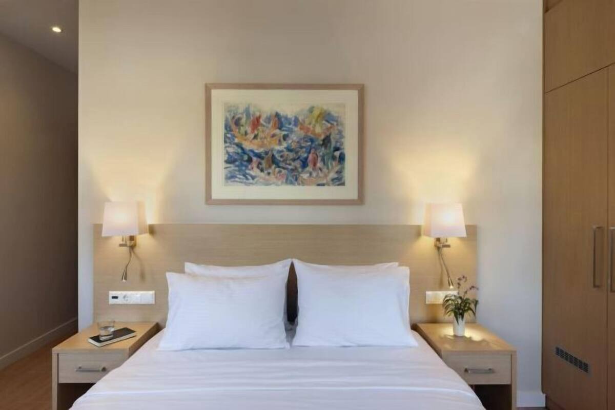 Ein Hotelzimmer mit einem großen Bett, zwei Nachttischen mit Lampen, einem Wandbild und einem Holzschrank.