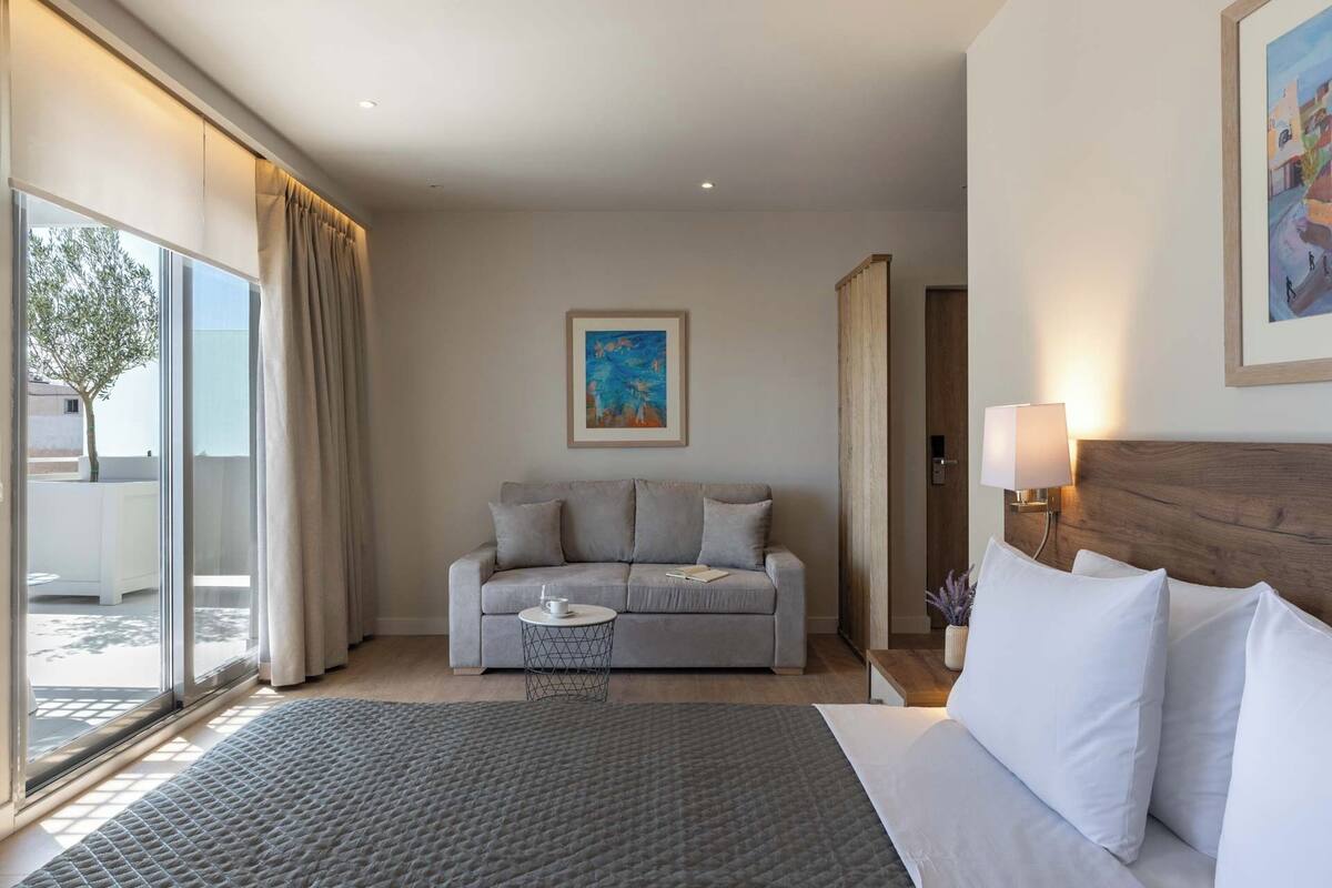 Ein Hotelzimmer mit einem Bett, einem grauen Sofa, einem kleinen Tisch und einem Bild an der Wand.