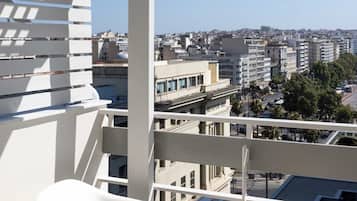 Un balcón con mobiliario blanco, una mesa con dos vasos de zumo de naranja y vistas a la ciudad.