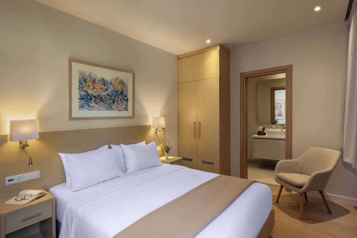 Ein Hotelzimmer mit einem großen Bett, Nachttischlampen, einem Kleiderschrank, einem Sessel und einem Bild an der Wand.