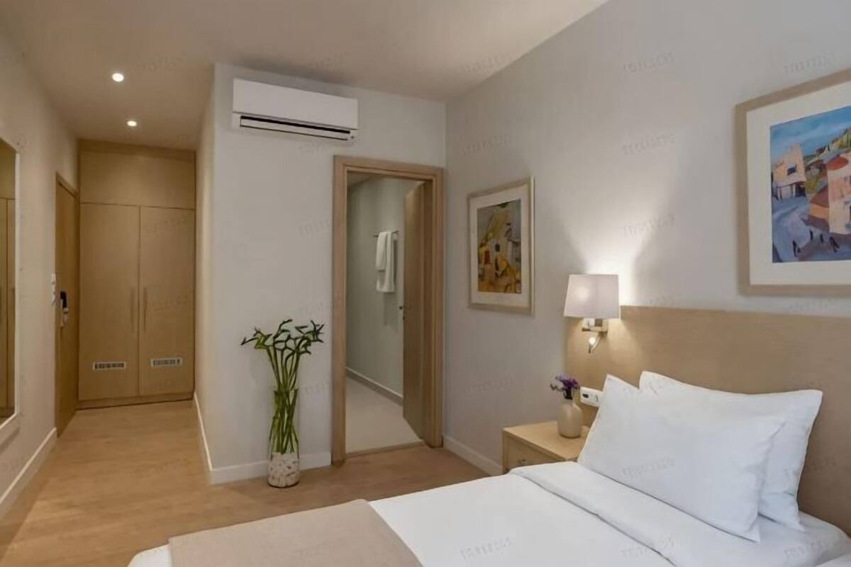 Ein Hotelzimmer mit Bett, Nachttisch, Lampe, Kunstwerk und Spiegel.