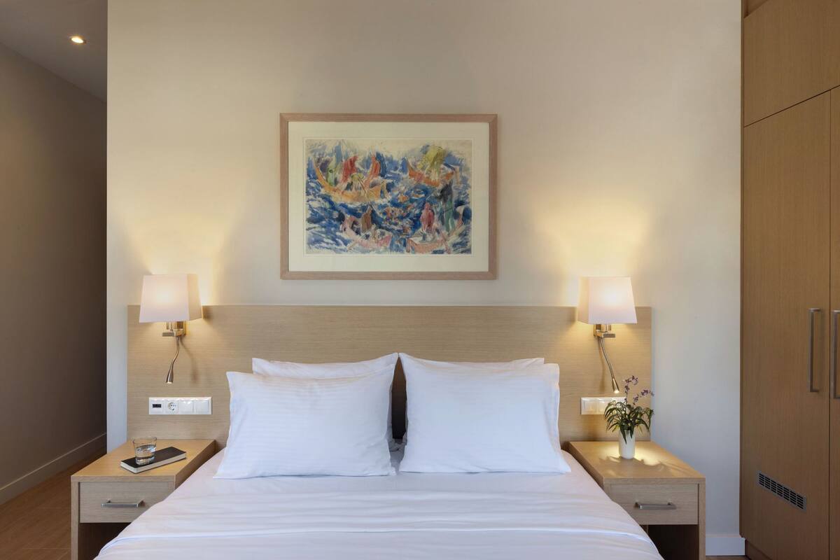 Ein Hotelzimmer mit einem großen Bett, zwei Nachttischen mit Lampen, einem Wandbild und einem Holzschrank.