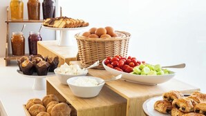 Una mesa de buffet con diversos alimentos, incluyendo pan, huevos, frutas y bollería.