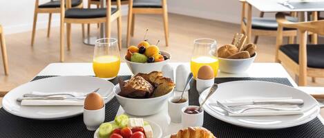 A breakfast setting with plates of croissants, eggs, and fruit, along with juice and bread.