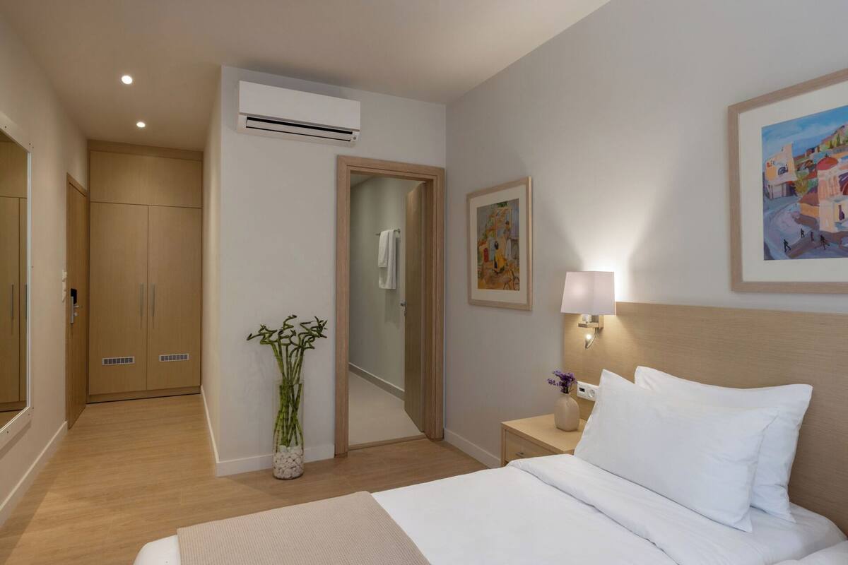 Ein Hotelzimmer mit Bett, Nachttisch, Lampe, Kunstwerk und einem Badezimmer mit Dusche und Toilette.