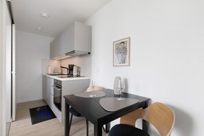 A compact kitchen with modern appliances, a dining table with two chairs, and a framed artwork on the wall.