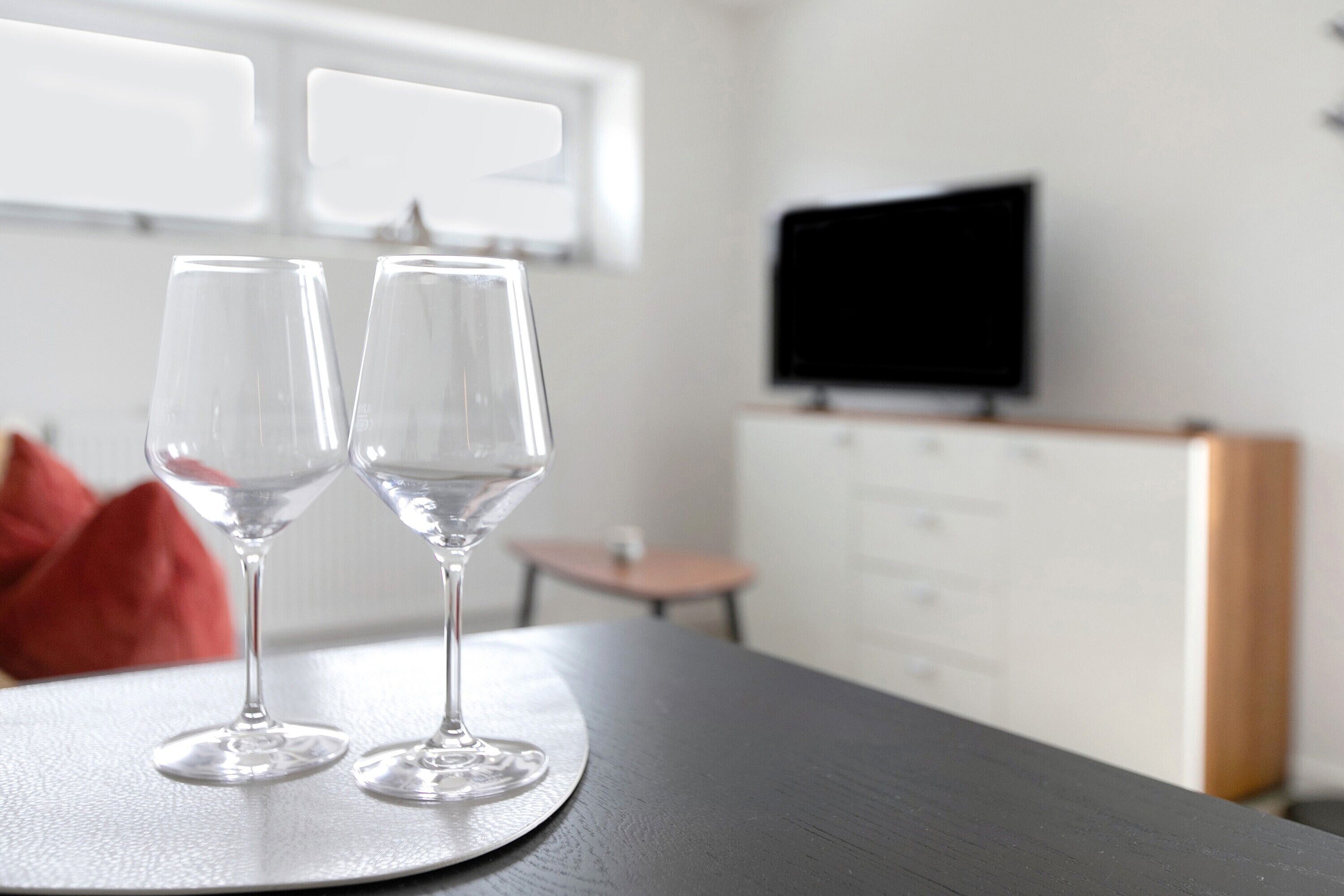 Dos copas de vino vacías sobre una mesa en una habitación con televisión y ventana.