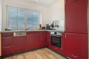 Cucina con pensili rossi, lavastoviglie, forno e finestra con vista.