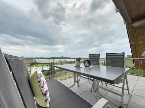 Un balcon avec une table, des chaises, un pot de fleurs et une vue sur la campagne.