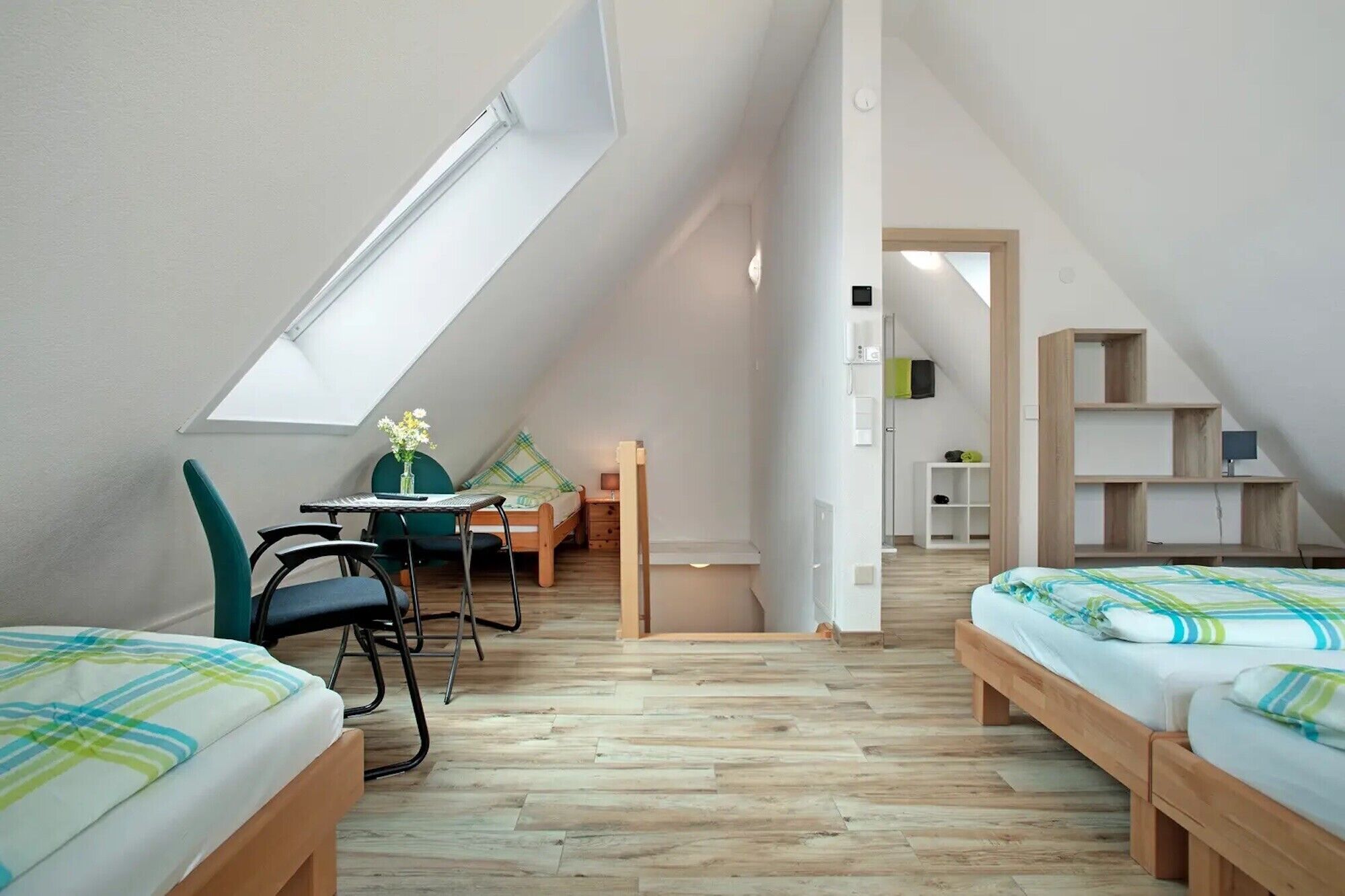 A small, well-lit attic bedroom with two beds, a desk, and a chair.