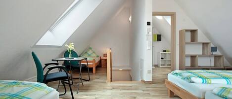 A small, well-lit attic bedroom with two beds, a desk, and a chair.