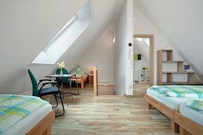 A small, well-lit attic bedroom with two beds, a desk, and a chair.