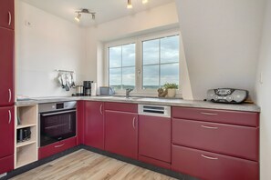 Une cuisine moderne avec des meubles de couleur rouge, un lave-vaisselle, un four et une grande fenêtre donnant sur un beau paysage.