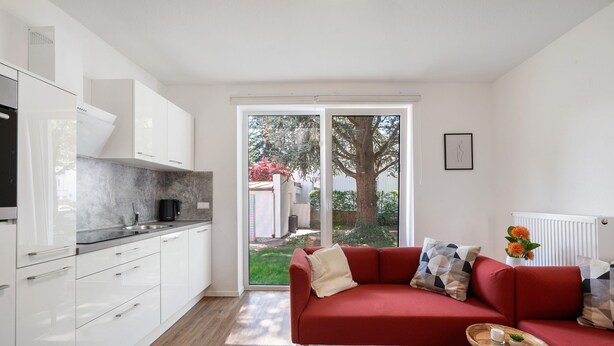 Una cocina moderna con armarios blancos, un sofá rojo y una pequeña mesa de madera.