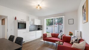 Una cocina moderna con armarios blancos, un sofá rojo y una mesa de comedor con sillas.