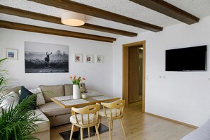 A modern living room with a sofa, a dining table with chairs, a TV mounted on the wall, and a large framed picture of a deer. - Studio 'Suite Home Seefeld' with Mountain View, Balcony and Wi-Fi (Seefeld in Tirol)