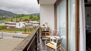 En balkong med utsikt över hus och berg, ett träräcke och en stol med en kudde.
