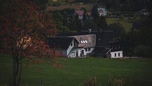 Een landelijk landschap met een huis, voorzien van een schuin dak en een klein bijgebouw.