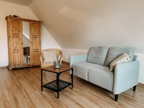 Une pièce avec un canapé bleu clair, un fauteuil en osier, une armoire en bois et une petite table noire.