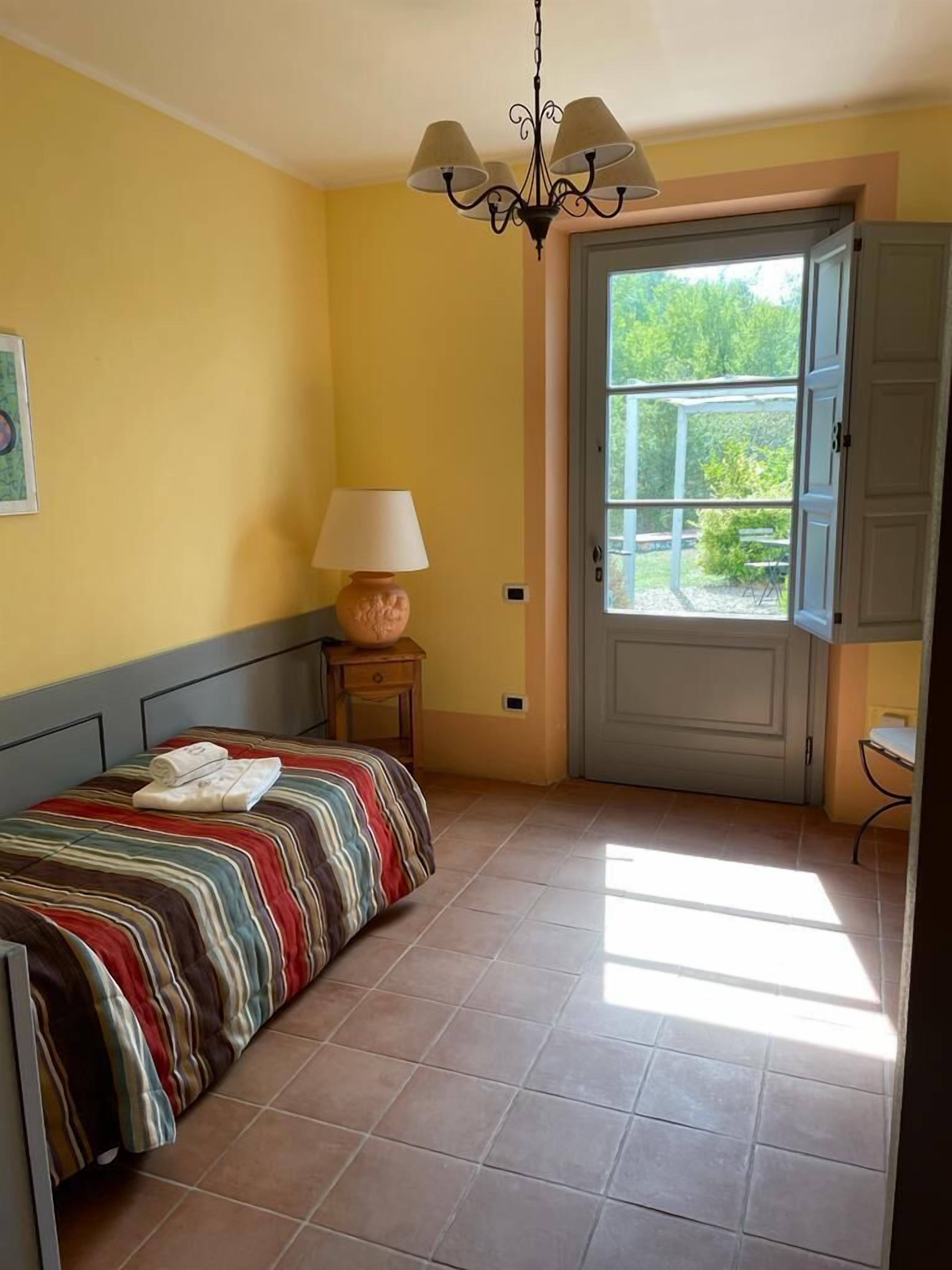 Quarto com cama, luminária, porta que dá para o exterior e janela.