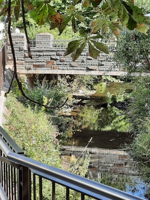 A stone bridge over a calm water body, surrounded by greenery and a stone wall.
