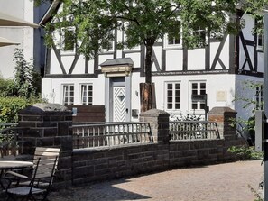 A traditional half-timbered building with a gated entrance, a stone wall, and a paved courtyard.