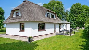 A house with a thatched roof, white walls, and a small patio with outdoor furniture.