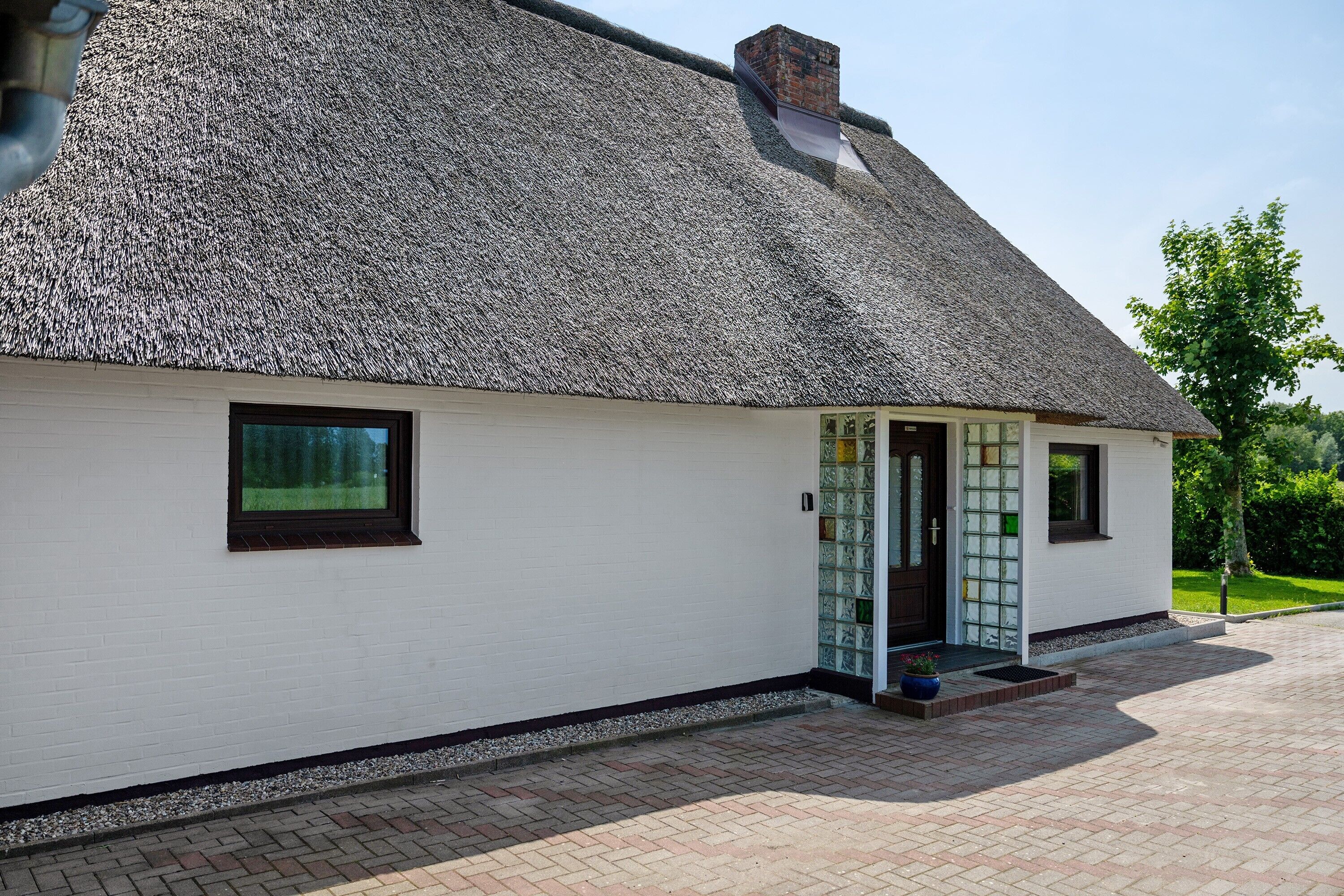 A white building with a thatched roof, a door with glass panels, and a brick pathway leading to the entrance.
