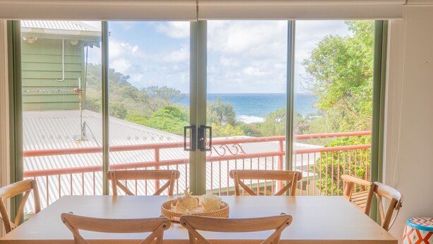 A dining area with a table and chairs, a view of the ocean, and a balcony with a railing.