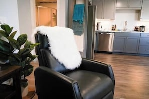 Relax in this stylish living room with a comfortable armchair, wooden floor, and a view of the modern kitchen area.