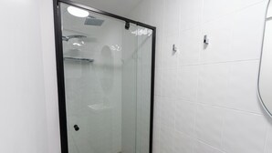 Un espace douche clos par des parois de verre, avec des murs recouverts de carreaux blancs et un cadre noir.