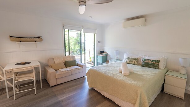 Une chambre à coucher comprenant un lit, un bureau, une chaise, un canapé, un ventilateur de plafond et une fenêtre.