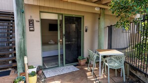 Un espace patio avec une table et des chaises en bois, une plante en pot et une porte-fenêtre coulissante donnant sur une pièce.