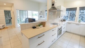 Une cuisine moderne avec des meubles blancs, un grand îlot central doté d’un évier et une hotte de cuisine en acier inoxydable.
